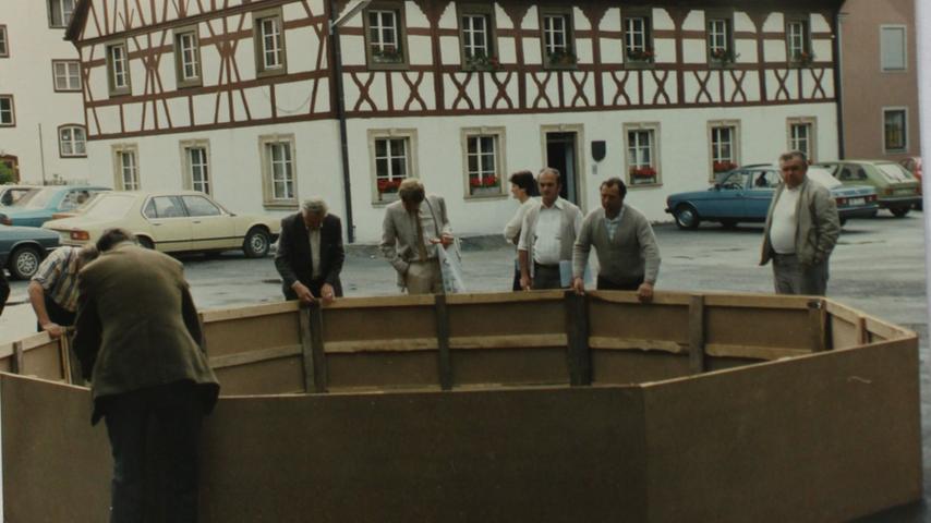 Ein Brunnen aus Pappe wird auf dem Marktplatz herumgetragen. Anhand des Modells stimmen die Bürger über den neuen Standort mit ab: 1984 wird er versetzt.