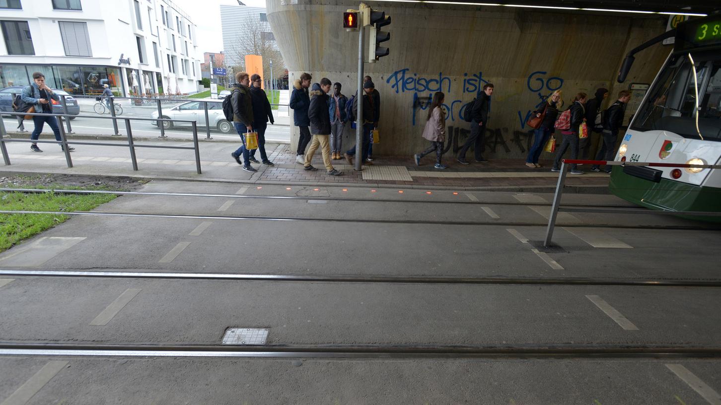 Das Foto der Stadtwerke Augsburg zeigt LED-Lichtsignale, die an zwei Haltestellenübergängen im Boden eingebaut sind. Rote LED-Leuchten entlang des Bordsteins am Übergang blinken, sobald das Fußgängersignal der Ampel auf Rot schaltet und sich eine Straßenbahn n