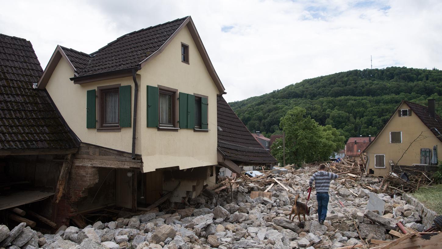 Ein junger Mann geht mit seinem Hund in Braunsbach (Baden-Württemberg) über eine Gerölllawine. Die Schäden nach dem Unwetter sind immens.