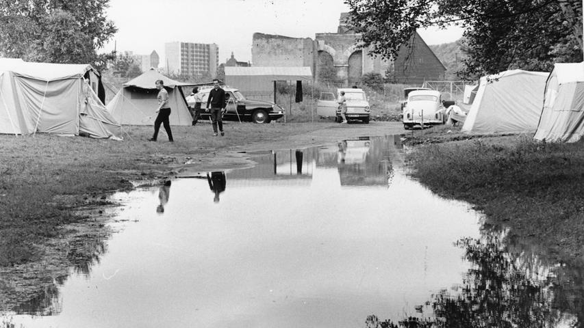 Noch braucht vom Campingplatz niemand "Land unter!" zu melden. Aber den Urlaubern bereitet der Regen keine Freude, zumal, wenn sich die Zelte und Wohnwagen im Wasser spiegeln.  Hier geht es zum Artikel vom 8. Juli 1966: Ein Sommer unterm Regenschirm.
