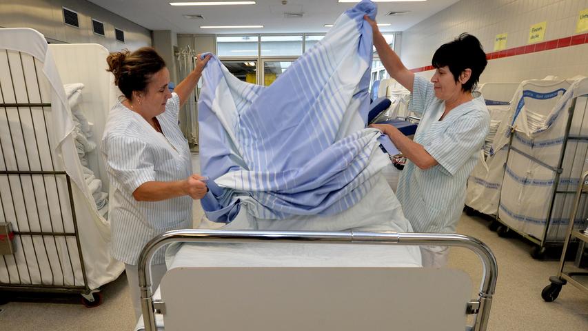 In der Bettenaufbereitung beziehen die Mitarbeiterinnen ein Bett, das frisch aus der Waschanlage gekommen ist.