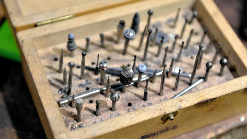 Pinzetten und andere filigrane Werkzeuge sind auf der Werkbank verstreut oder in kleinen Kästchen sortiert.