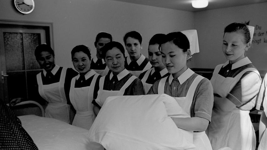 So schütteln sie die Betten alle Tage: Gwi Kook Lie, Kong Soon Yang, Tai Re Lie, Hea Rang Oh (v. re. n. li.). Im Hintergrund die deutsche Mitschülerinnen, die von Oberschwester Fanny Schramm als Lehrschwester unterrichtet werden. Die Krankenpflegeschule leitet Schwester Erna, von den Koreanerinnen "Mutti" genannt. Sie betreut 23 Schülerinnen. 
 
  Hier geht es zum Artikel vom 13. September 1966: Lächeln als Medizin.