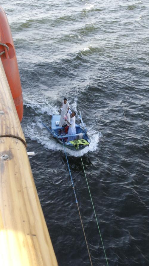 Geschickt machen die beiden Insassen ihr kleines Boot am großen Kreuzfahrtschiff mit Seilen fest.