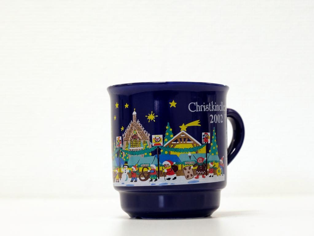 Eine dunkelblaue Tasse, gemalt mit bunten Motiven von Weihnachts- und Schneemännern über die Frauenkirche und Christkindlesmarkt-Buden gab es im Jahr 2002. Eine dunkelblaue Tasse, gemalt mit bunten Motiven von Weihnachts- und Schneemännern über die Frauenkirche und Christkindlesmarkt-Buden gab es im Jahr 2002.