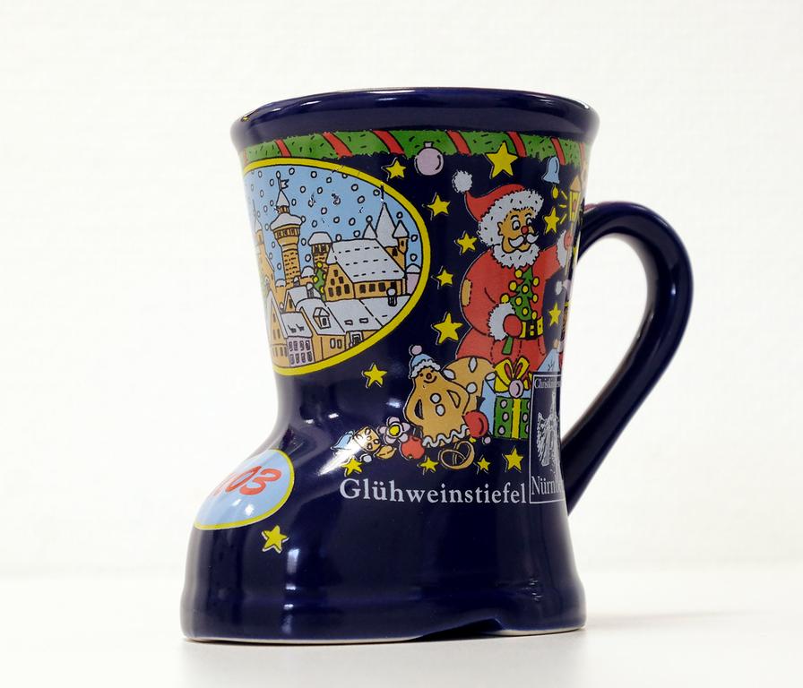 Dunkelbau, mit hellblauen Details, einem Weihnachtsmann und weiteren schön gemalten Motiven: So erschien die Tasse im Stiefel-Design im Jahr 2003. In diesem Jahr trat das Design des Glühweinstiefels zum ersten Mal auf, um etwas Neues zu kreiieren.  Dunkelbau, mit hellblauen Details, einem Weihnachtsmann und weiteren schön gemalten Motiven: So erschien die Tasse im Stiefel-Design im Jahr 2003. In diesem Jahr trat das Design des Glühweinstiefels zum ersten Mal auf, um etwas Neues zu kreiieren.