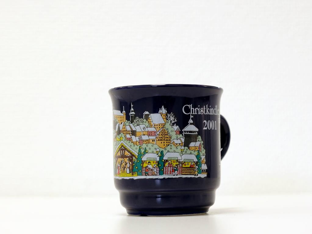 Im Vorjahr zierten die Tasse weniger Farben. Auf einer ebenfalls dunkelblauen Tasse waren etwas mehr Buden, die Burg und viele andere Gebäude zu sehen. Auch eine Krippe war auf der Tasse abgebildet.  Im Vorjahr zierten die Tasse weniger Farben. Auf einer ebenfalls dunkelblauen Tasse waren etwas mehr Buden, die Burg und viele andere Gebäude zu sehen. Auch eine Krippe war auf der Tasse abgebildet.