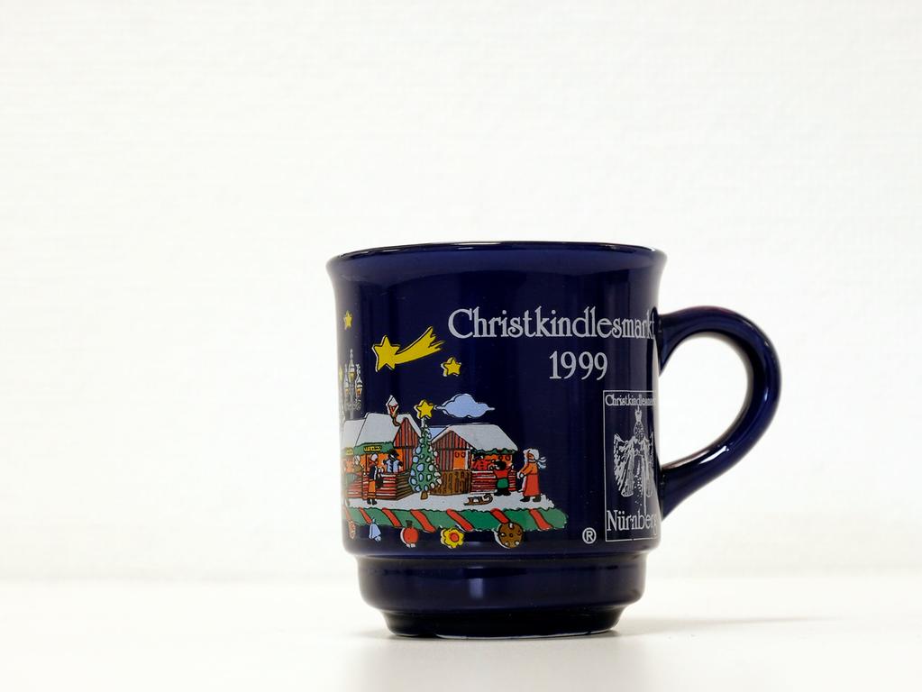 Auf einer dunkelblauen Tasse aus dem Jahr 1999 waren neben vielen schneebedeckten Buden die Frauenkirche sowie der Schöne Brunnen in bunten Farben abgebildet. Auch kleine Sterne, eine Sternschnuppe sowie ein sichelförmiger Mond zierten die Oberfläche der Tasse. In diesem Jahr gab es die erste Kinderweihnacht auf dem Nürnberger Christkindlesmarkt. Auf einer dunkelblauen Tasse aus dem Jahr 1999 waren neben vielen schneebedeckten Buden die Frauenkirche sowie der Schöne Brunnen in bunten Farben abgebildet. Auch kleine Sterne, eine Sternschnuppe sowie ein sichelförmiger Mond zierten die Oberfläche der Tasse. In diesem Jahr gab es die erste Kinderweihnacht auf dem Nürnberger Christkindlesmarkt.
