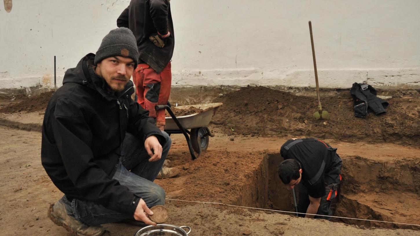 Grabungsleiter Matthias Tschuch zeigt Fundstücke, während seine Kollegen das Erdreich untersuchen.