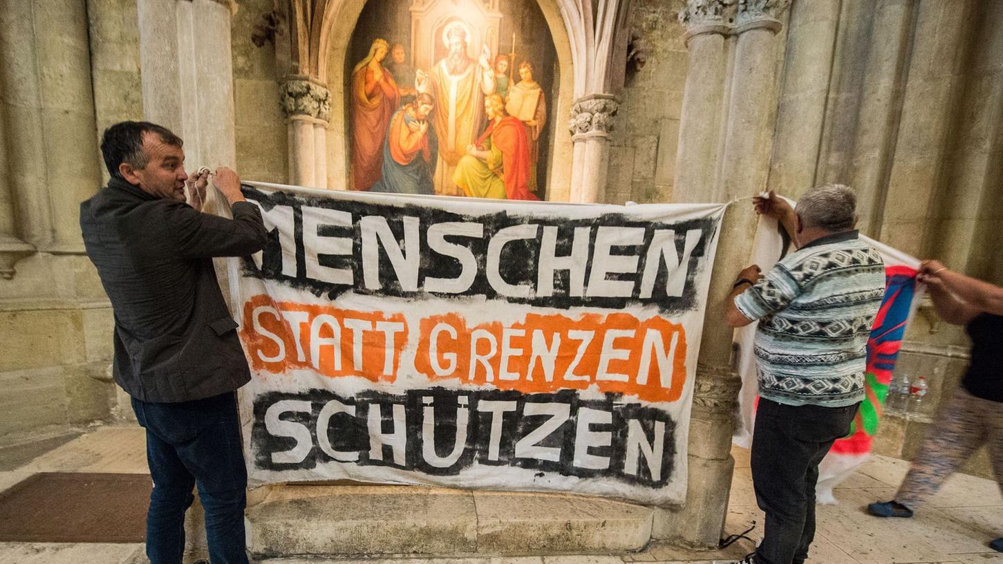Flüchtlinge hängen im Dom St. Peter in Regensburg ein Transparent mit der Aufschrift "Menschen statt Grenzen schützen" auf: Kirchenasyl bleibt politisch hoch umstritten.