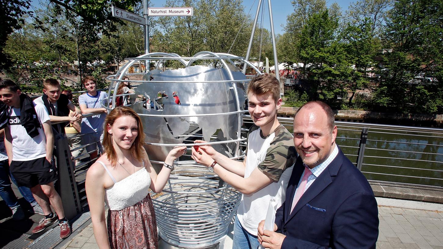 Eine Skulptur neben der Brücke soll nun für die Schlösser herhalten: Ein Liebespaar der Schule durfte sich als erstes daran verewigen - unterstützt von Bürgermeister Christian Vogel.