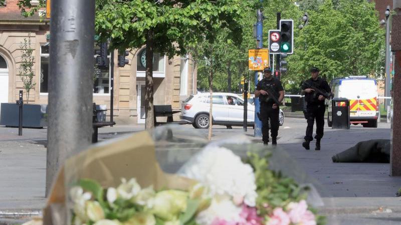 Zum Gedenken der Opfer liegen in Manchester Blumen aus, im Hintergrund pa­t­rouil­lie­ren Polizisten.