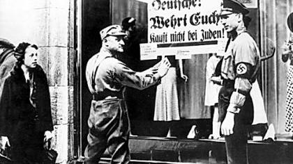 Die Folgen des Rassenwahns: SA-Männer kleben ein Plakat mit der Aufschrift «Deutsche! Wehrt Euch! Kauft nicht bei Juden» an die Schaufensterscheibe eines Geschäfts. Die Folgen des Rassenwahns: SA-Männer kleben ein Plakat mit der Aufschrift «Deutsche! Wehrt Euch! Kauft nicht bei Juden» an die Schaufensterscheibe eines Geschäfts.