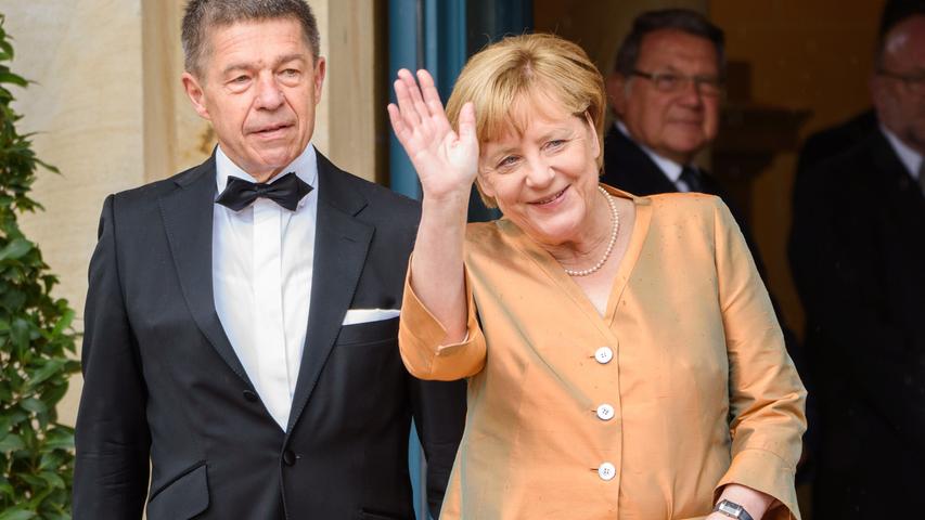 Die Bundeskanzlerin wird von ihrem Mann Joachim Sauer begleitet und winkt den Zaungästen zu.