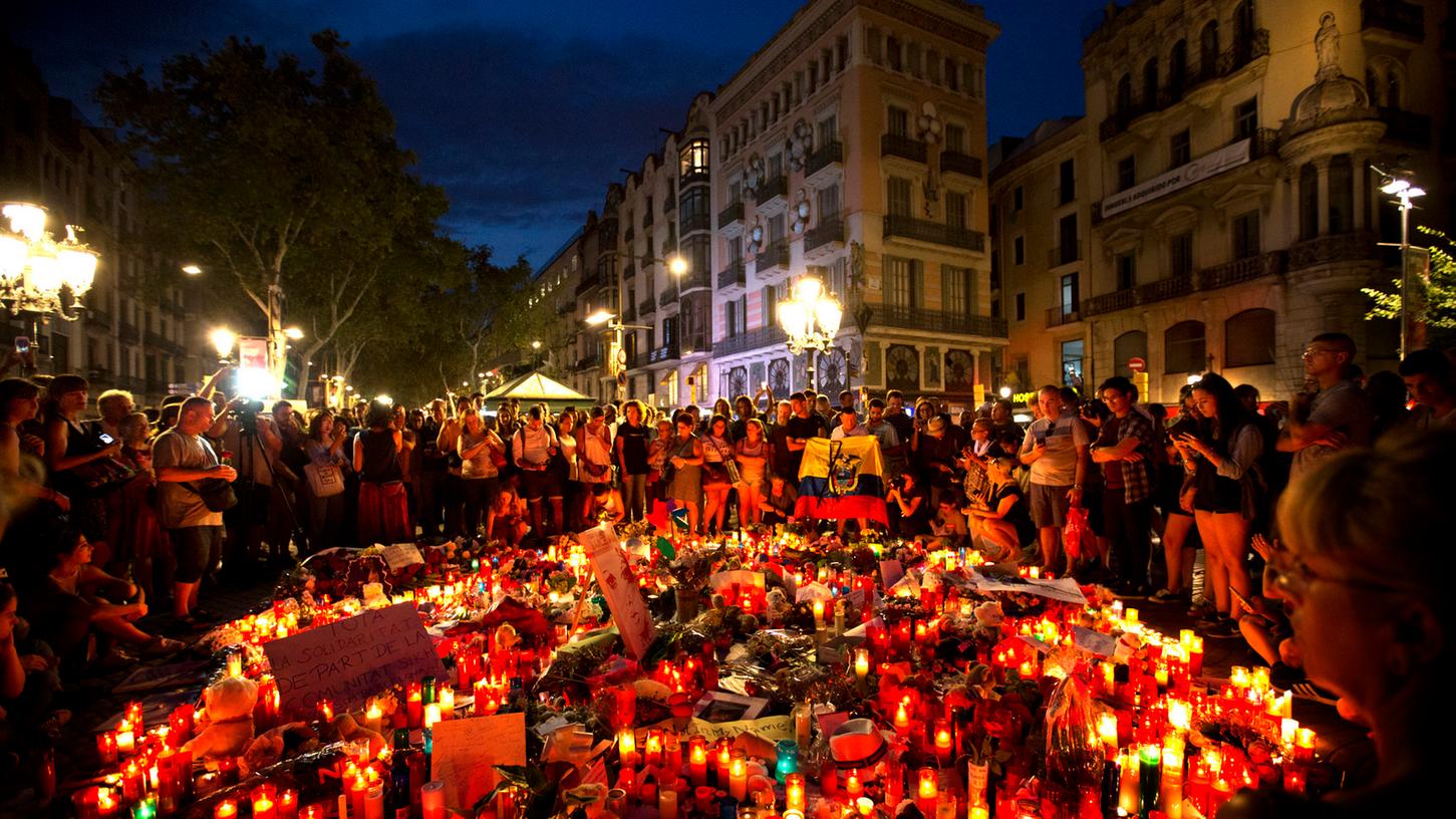 Menschen umringen am Freitagabend niedergelegte Blumen und Kerzen auf der Flaniermeile Las Ramblas in Barcelona.