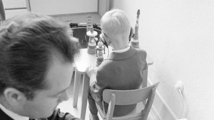 Bei der audiographischen Prüfung: Oberlehrer Axmann vermittelt dem schwerhörigen Kind mit einem Knopfdruck (links) verschieden hohe Töne. Sobald der Bub einen Laut wahrnimmt, fügt er ein Element auf den Spielzeugturm.  Hier geht es zum Kalenderblatt vom 22. September 1967: Ein Test schadet nicht