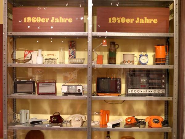 Eine Vitrine mit echten Gebrauchsgegenständen wie Telefon oder Warmhaltekanne — in der damals beliebten Signalfarbe Orange — macht deutlich, dass die Puppenhäuser auch damals ein Abbild des Zeitgeists waren.