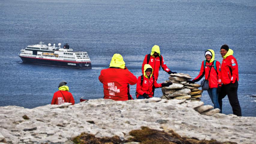 Passagiere klettern über Felsen auf einer Falklandinsel. Dahinter liegt die MS Midnatsol.