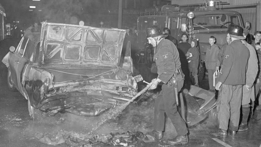 Die Feuerwehrmänner löschen die brennenden Wrackteile des Wagens. Zuvor war ein betrunkener Fahrer in die wartende Fahrzeugkolonne vor einer Ampel gerast.  Hier geht es zum Kalenderblatt vom 3. Dezember 1967: Ein brennendes Auto explodierte