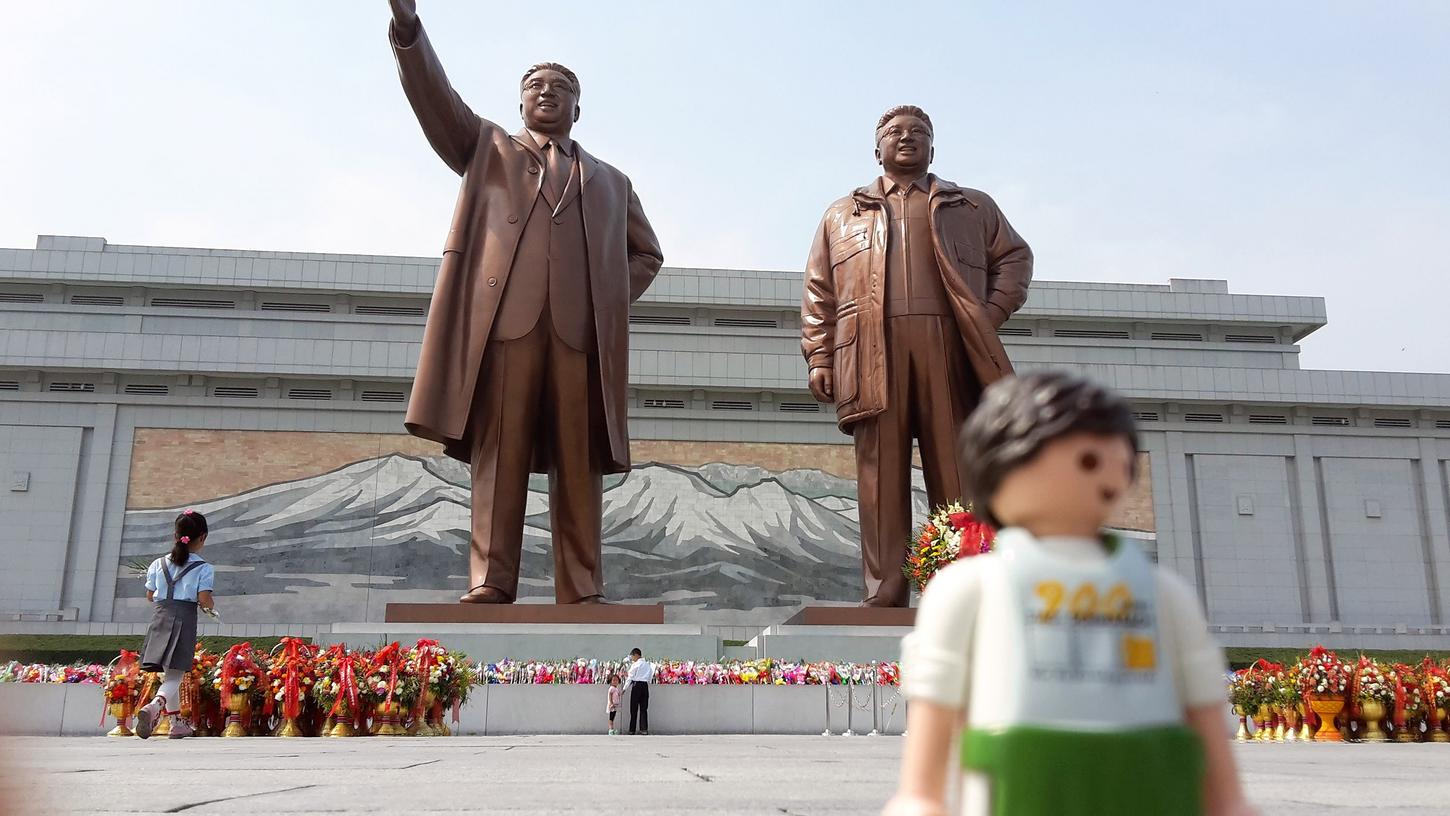 Reisefreiheit? Zumindest für Plas­tik-Männchen: Der „Playmomoo“ vor den 20 Meter hohen Bronzefiguren von Kim Il-sung und Kim Jong-il in Pjöngjang.  Der Schwabacher Mini-Goldschläger hat es dank Stefan Schwenk sogar nach Nordkorea geschaft, eines der mysteriösesten Länder dieser Welt.