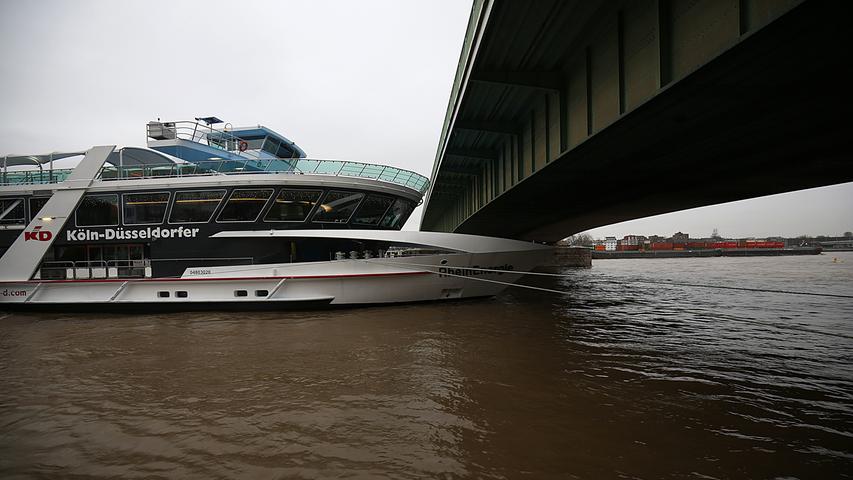 Ein Schiff liegt am 04.01.2018 in Köln (Nordrhein-Westfalen) am Rheinufer vor einer Brücke. Das Wasser im Fluss Rhein steht ungewöhnlich hoch. Manche Schiffe passen nicht mehr unter den Brücken hindurch.
