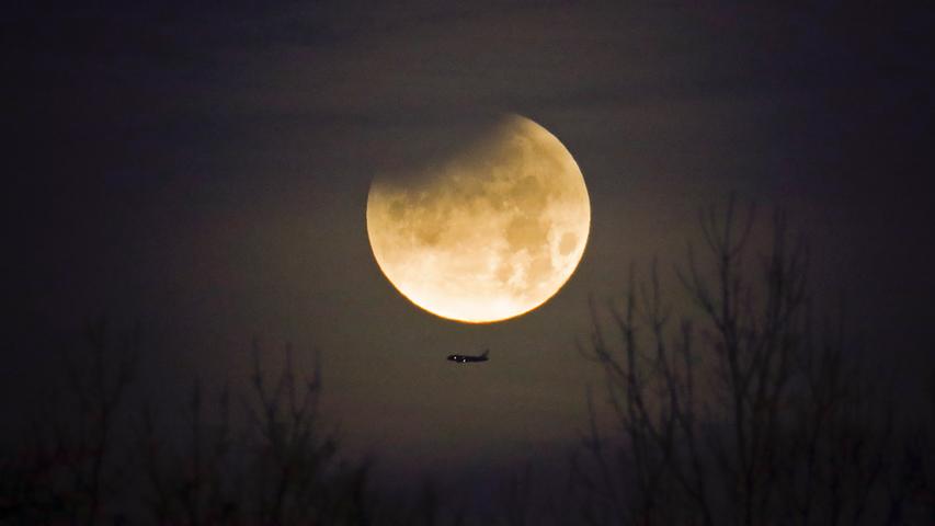 Ein Flugzeug fliegt im US-amerikanischen Charlotte am Mond vorbei, der in einer seltenen Kombination aus Supermond, Blutmond und Mondfinsternis am Himmel steht.