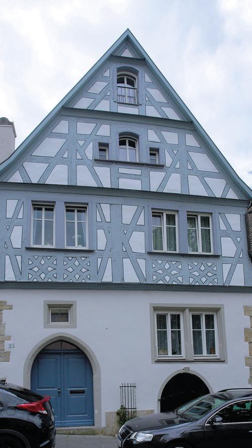 Die Rothenburger Herrngasse führt vom Burgtor zum Marktplatz und wird gesäumt von einer ganzen Reihe prächtiger Patrizierhäuser sowie von kleineren Wohnhäusern aus unterschiedlichen Zeiten. Das giebelständige, zweigeschossige Wohnhaus Nr. 25 zeichnet sich durch sein Schmuckfachwerk in den Obergeschossen über einem gemauerten Sockelgeschoss aus. Die Entstehungszeit ist mit 1590 angegeben. Der Gewölbekeller allerdings stammt noch vom Vorgängerbau und ist somit deutlich älter. Das Fachwerk konnte hingegen einheitlich dendrochronologisch einheitlich auf 1706 datiert werden. Weite Teile der Innenausstattung gehen auf eine Umgestaltung im 19. Jahrhundert zurück.