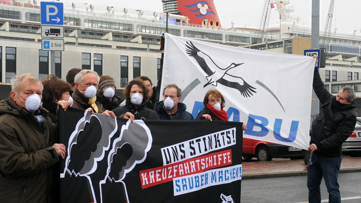 Mitglieder des Naturschutzbundes NABU weisen vor dem Kreuzfahrtterminal in Bremerhaven auf die Umweltbelastung durch Kreuzfahrtschiffe hin. Im Hintergrund ist der Kreuzfahrtschiff-Neubau «Disney Fantasy» als ein Vertreter der ganz großen Klasse von Passagierschiffen an der Columbuspier zu erkennen. Der NABU fordert unter anderem Rußfilter, schwefelarmen Diesel und Landstromanschluss für Ozeanriesen. Mitglieder des Naturschutzbundes NABU weisen vor dem Kreuzfahrtterminal in Bremerhaven auf die Umweltbelastung durch Kreuzfahrtschiffe hin. Im Hintergrund ist der Kreuzfahrtschiff-Neubau «Disney Fantasy» als ein Vertreter der ganz großen Klasse von Passagierschiffen an der Columbuspier zu erkennen. Der NABU fordert unter anderem Rußfilter, schwefelarmen Diesel und Landstromanschluss für Ozeanriesen.