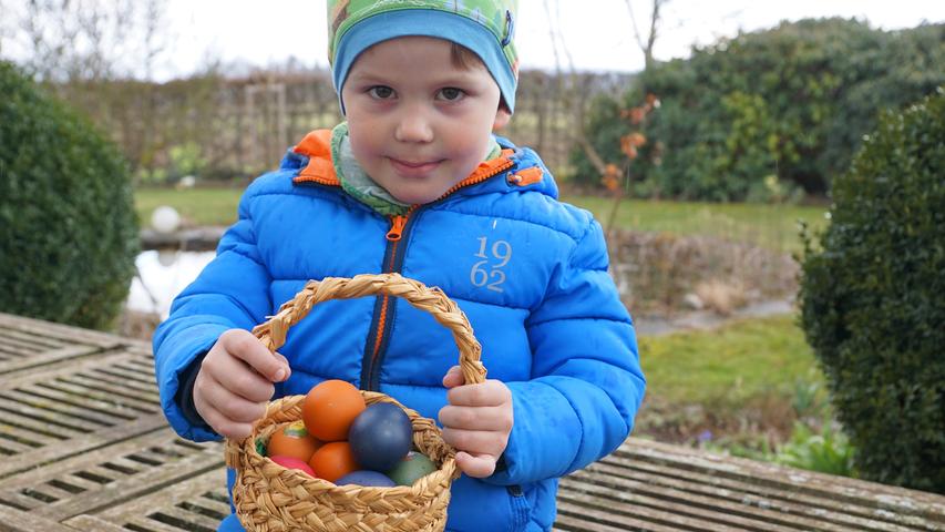 Ein Körbchen voller bunt gefärbter Eier hat der kleine Clemens im Garten gefunden.