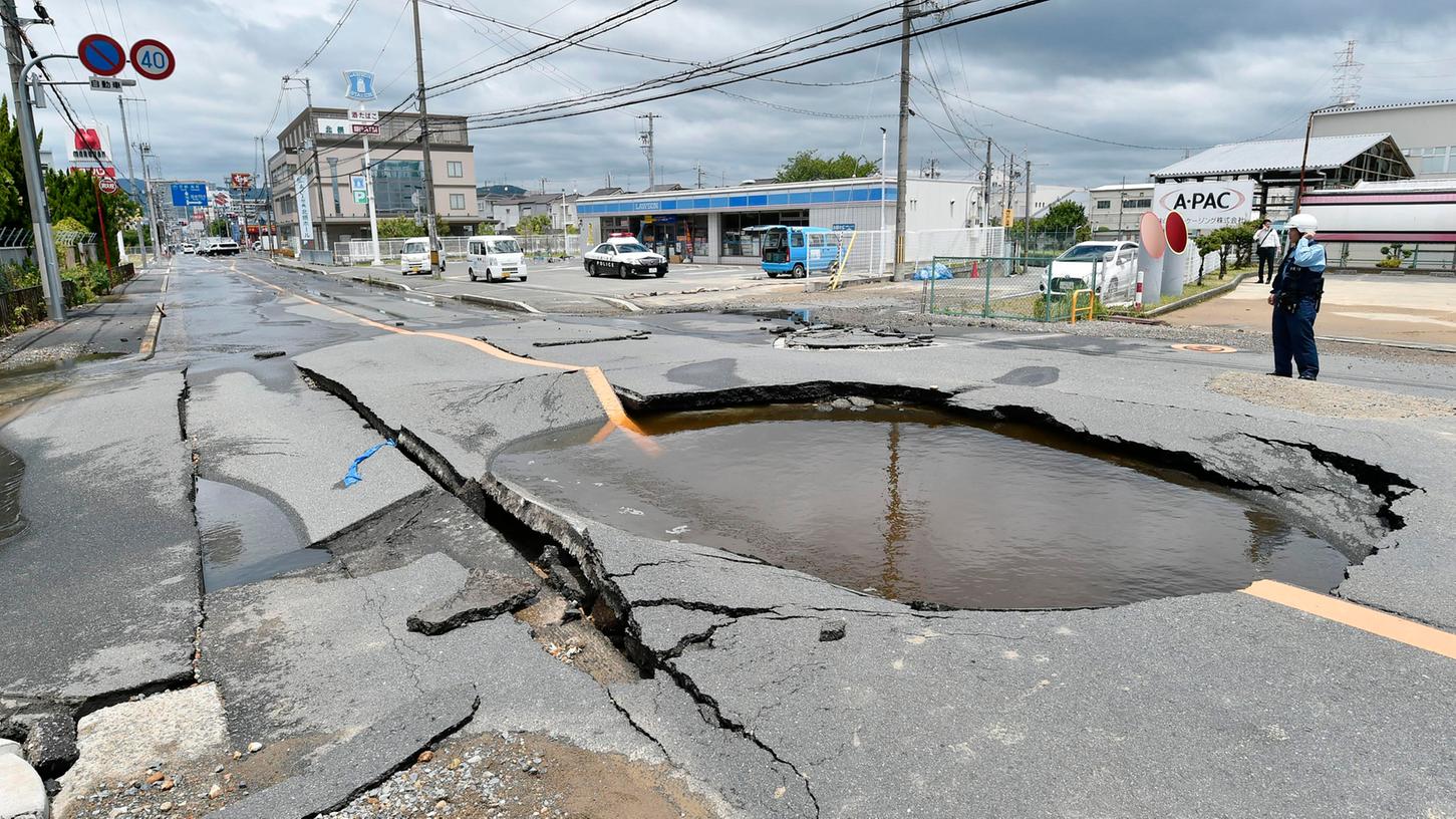 Ein mit Wasser gefüllter Krater auf einer Straße, nachdem Wasserrohre nach einem Erdbeben gebrochen waren. Bei einem starken Erdbeben im Westen Japans sind am Montag mindestens drei Menschen ums Leben gekommen.