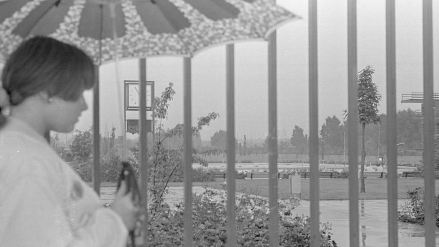 Unterm Regenschirm: wehmütig schaut diese junge Dame durch das Gitter in das Freibad West. Hier geht es zum Kalenderblatt vom 21. Juni 1968: Fällt der Sommer ins Wasser?