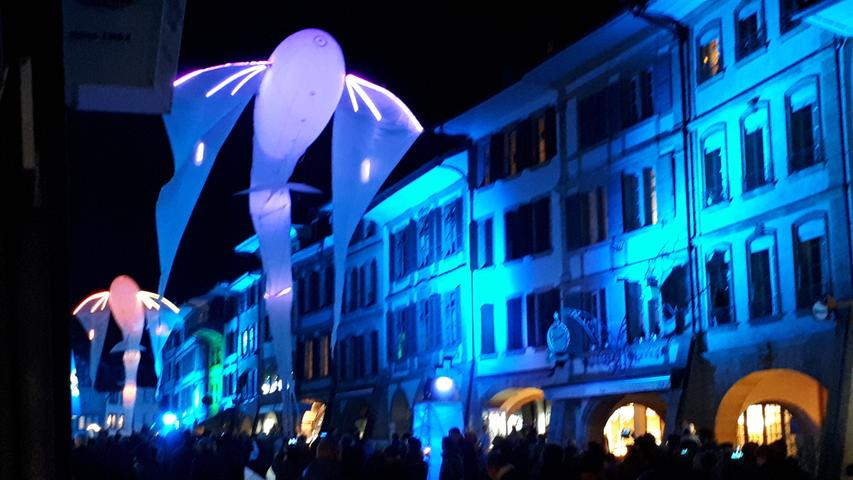 Drachen und andere luftige Wesen schweben beim Licht-Festival durch die Hauptstraße von Murten.