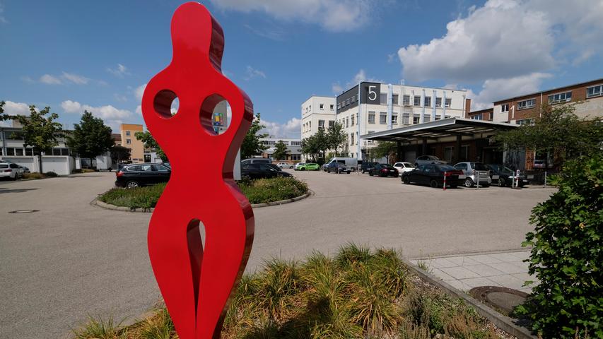 Empfangsdame in Rot: An der Einfahrt von der Löffelholzstraße zum nördlichen Komplex mit einem Sanitärgroßhandel, der Tischmanufaktur und dem "Aufgetischt" begrüßt eine Skulptur die Beschäftigten und Besucher.