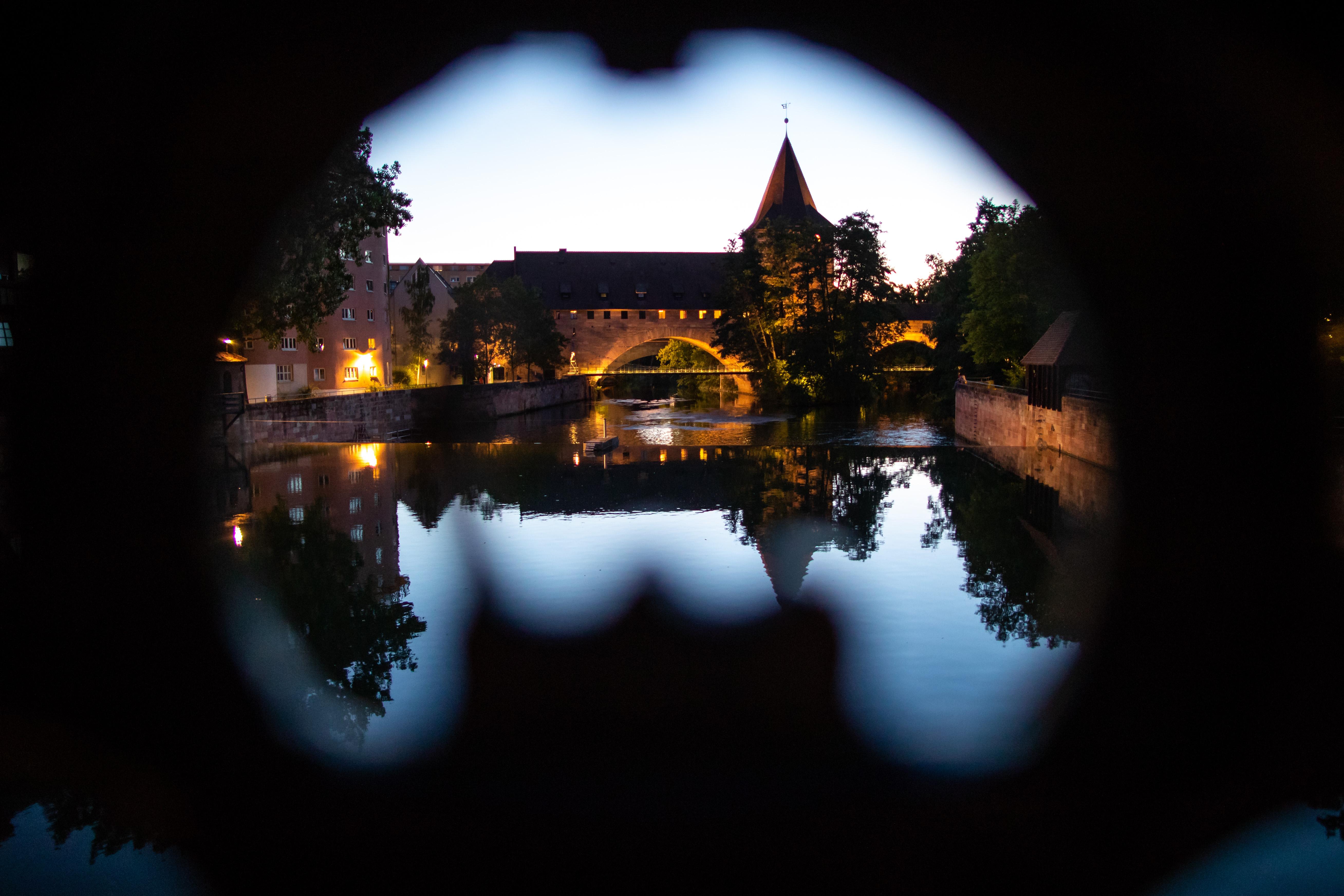 Der Schlayerturm mit dem Kettensteg an der Pegnitz am Hallertor, betrachtet durch das Geländer von der Maxbrücke.