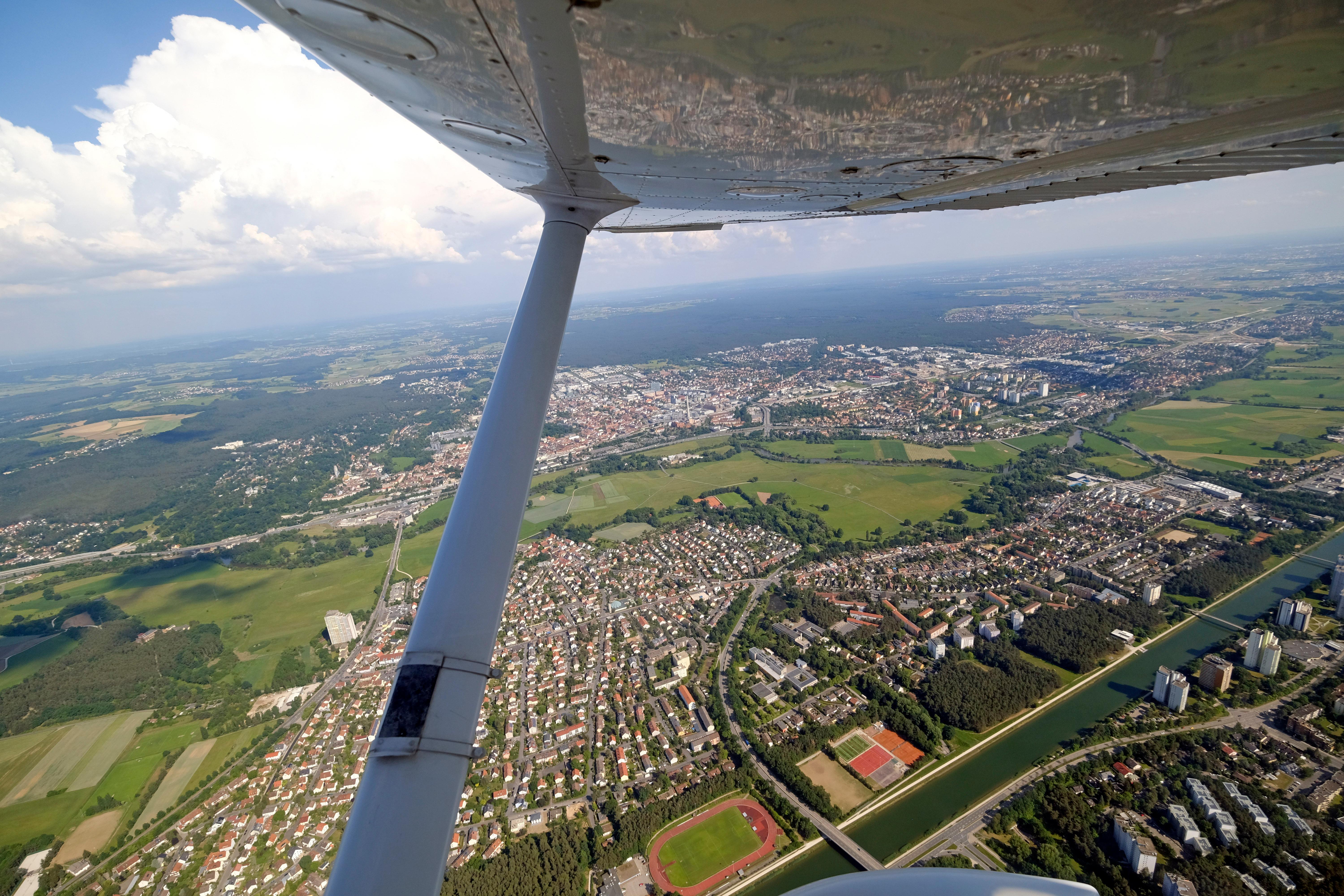 Erlangen zeigt sich aus dem Flugzeug in verschiedenen Facetten: Einmal wie eine Spielzeugstadt unten auf dem Erdboden, aber auch als kecke Spiegelung im Flügel.