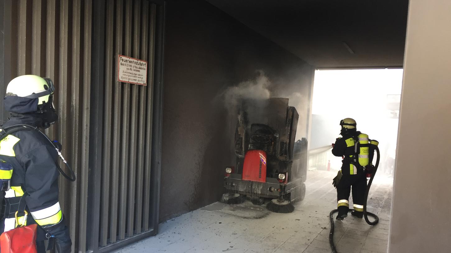 Feuerwehrmänner löschen die brennende Kehrmaschine ab.