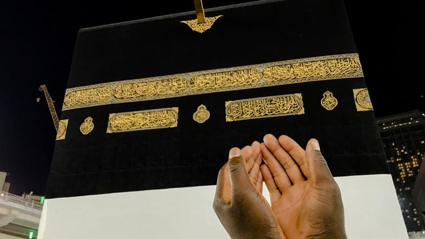Ein muslimischer Pilger betet vor der Hadsch und reckt dabei seine Hände in Richtung Kaaba.