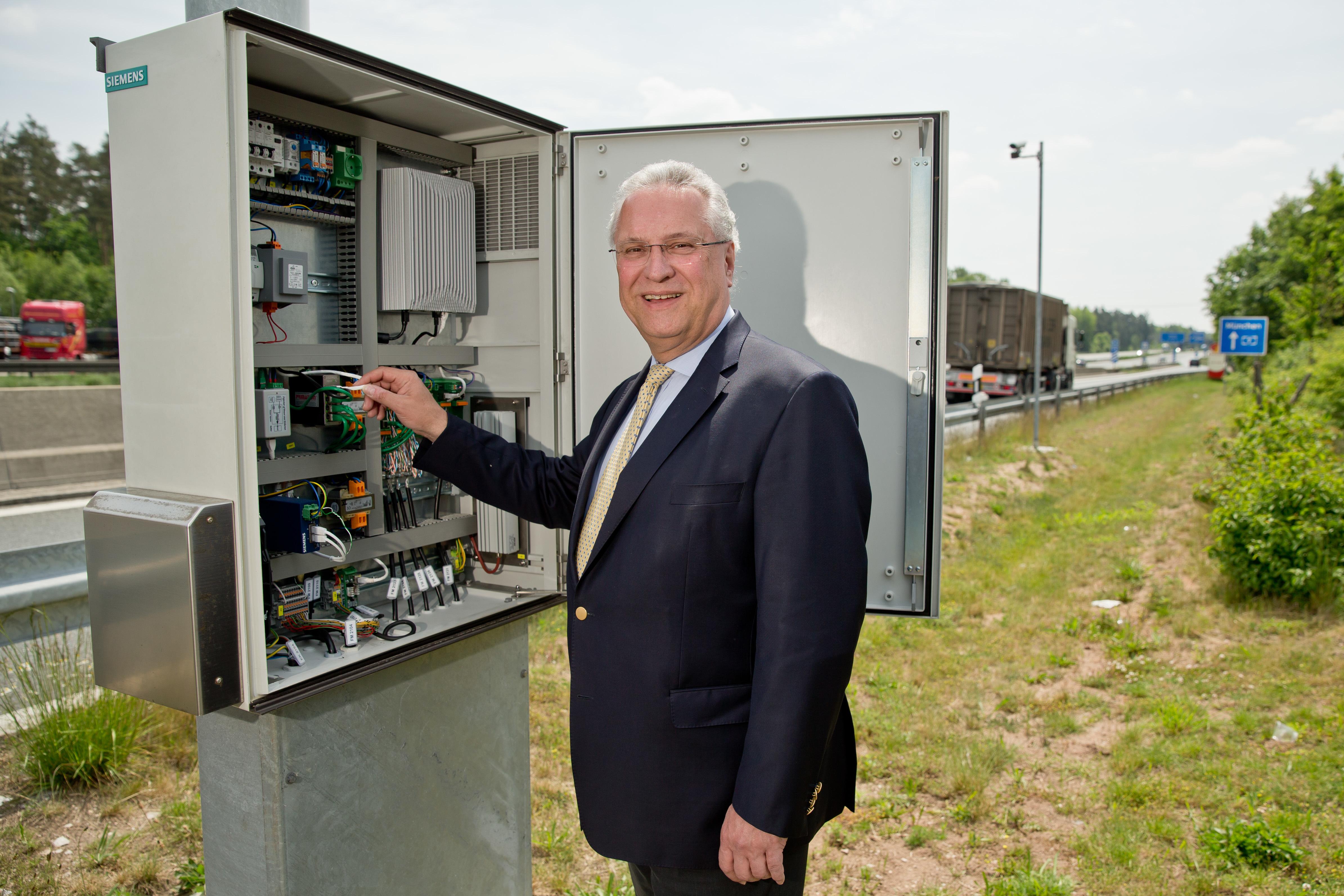 Der bayerische Innenminister Joachim Herrmann (CSU), steht am 2015 in Nürnberg auf einem Rastplatz entlang der Autobahn Nürnberg-München (A9) an einem Schaltschrank ein neues elektronischen Leitsystem für Lkw vor...