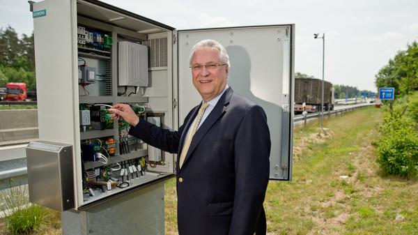 Der bayerische Innenminister Joachim Herrmann (CSU), steht am 2015 in Nürnberg auf einem Rastplatz entlang der Autobahn Nürnberg-München (A9) an einem Schaltschrank ein neues elektronischen Leitsystem für Lkw vor...