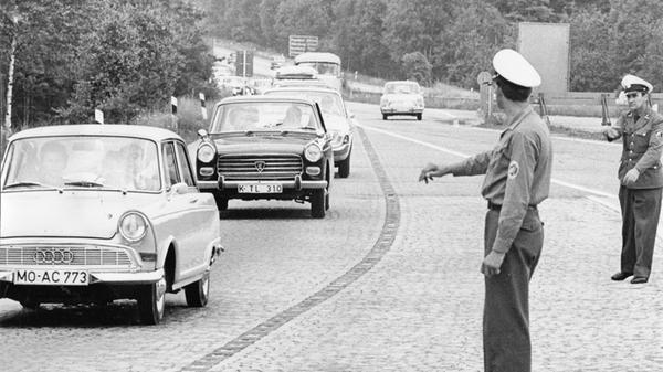 An einem Samstagvormittag im Juli 1965 waren diese Autos auf dem "Nürnberger Kreuz" der Autobahnen 3 und 9 Richtung München unterwegs. Man beachte das Kopfsteinpflaster der Ausfahrtsfahrbahn. Die Polizeibeamten waren vor Ort, um den Verkehrsfluss zu überwachen. Ihre Signale an die Autofahrer, zügiger zu fahren, seien oft vergeblich gewesen, ist überliefert. Ein DKW F12 führt auf diesem Bild die Karawane an, gefolgt von einem Peugeot 404 und einem (Ford) Taunus 17M.