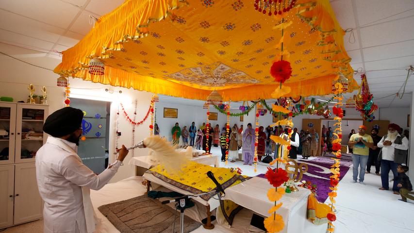 Im Gebetsraum ist ein goldener Himmel aufgespannt. Ein Priester rezitiert aus dem heiligen Buch der Sikhs, die Gläubigen hören zu.