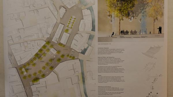 Die Architekten haben sich gegen eine Parzellierung entschieden, wollen dem Platz eher einen Rahmen geben. Baumreihen längs des Platzes, sowohl auf der Nord- als auch auf der Südseite dominieren diesen Entwurf. Die Mitte des Platzes bleibt komplett frei. Der Tiefgaragen-Eingang wird zum überdachten Wartebereich. Was den Bodenbelag betrifft, arbeiten alle Architekten mit hochwertigen Natursteinen, die zum Marktplatz weitergeführt werden, um beide Plätze zu verbinden.