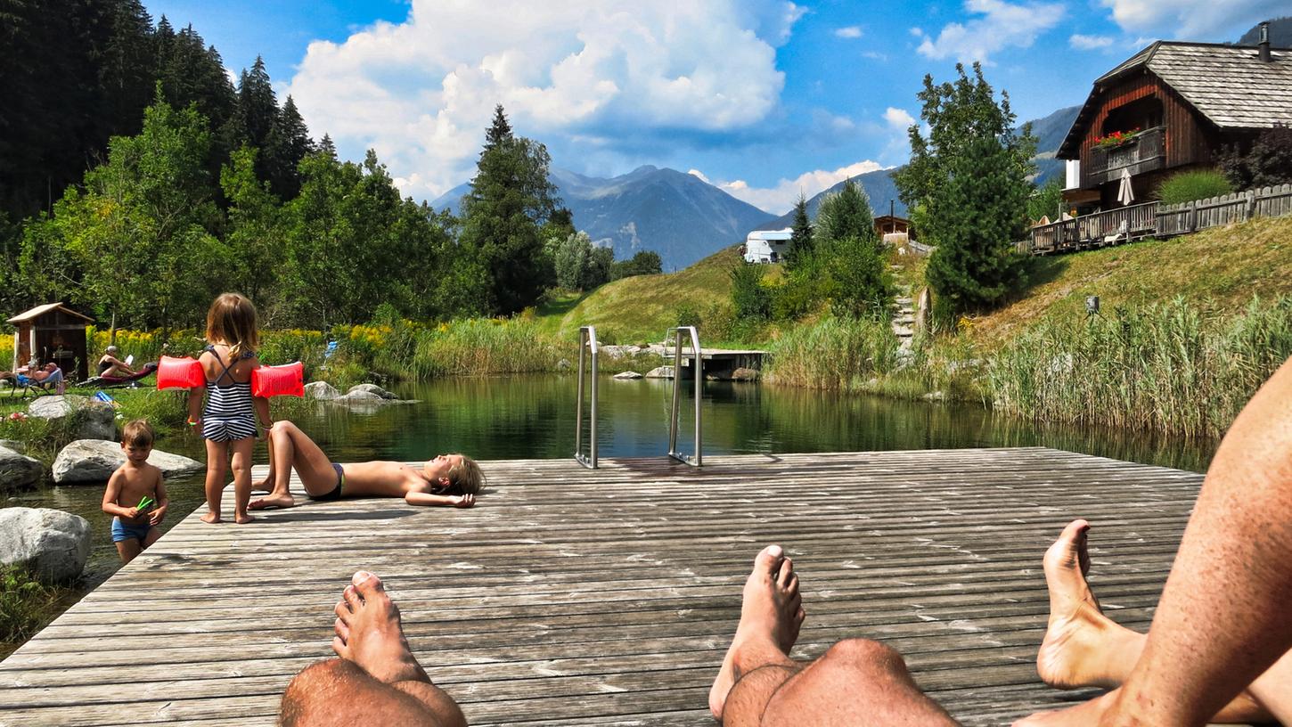Entspannt mit der Familie an einem Badeteich in den Bergen - entschleunigender Urlaub, wie ihn viele nach Corona haben wollen.