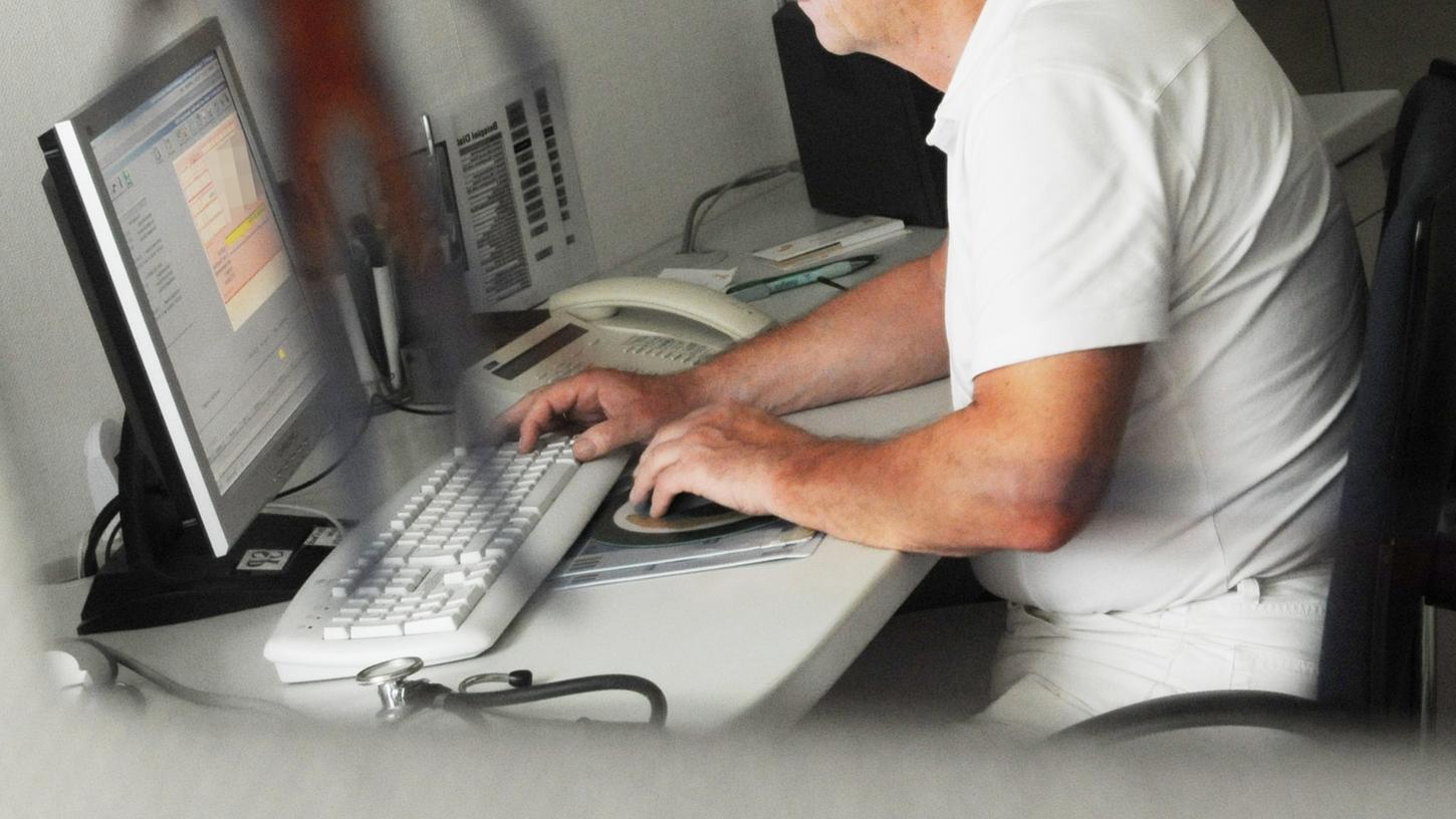 Ein Arzt sitzt in seiner Praxis an einem Computer (Symbolbild). 
