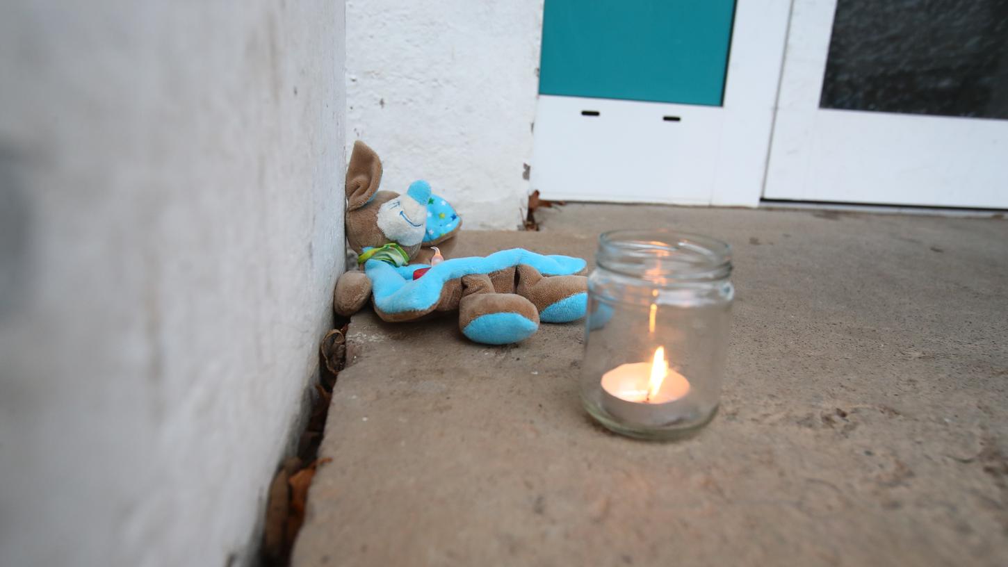 Ein Teddy liegt neben einem Teelicht im Eingangsbereich eines Wohnhauses im Stadtteil Winzerla. Hier wurden am Montag in einer Wohnung die Leichen von vier Menschen gefunden. Angaben der Staatsanwaltschaft zufolge handelt es sich bei dem Säugling um das leibliche Kind des mutmaßlichen Täters.