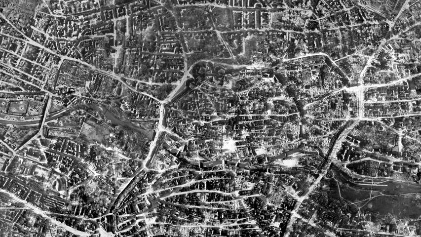 Am Ende des Krieges sieht das völlig anders aus. Die Nürnberger Altstadt liegt in Trümmern. Auf praktisch keinem der fotografierten Häuser ist mehr ein Dach zu sehen, tausende Gebäude sind nur noch Ruinen. Vor allem entlang der Pegnitz und an der Bahnstrecke am unteren Bildrand sind überall Bombenkrater zu erkennen.