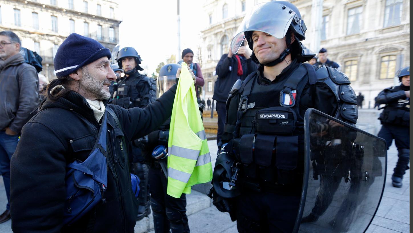 Ein Demonstrant der "Gilets Jaunes" (Gelbwesten) versucht, einem Polizisten während der Demonstration eine gelbe Warnweste zu geben.