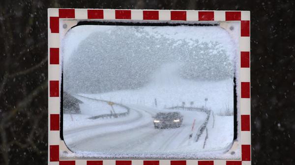 Die Schneemassen haben auch das Ostallgäu erreicht: Ein Auto fährt über eine eingeschneite Straße im Luftkurort Nesselwang am Rande der Allgäuer Alpen.