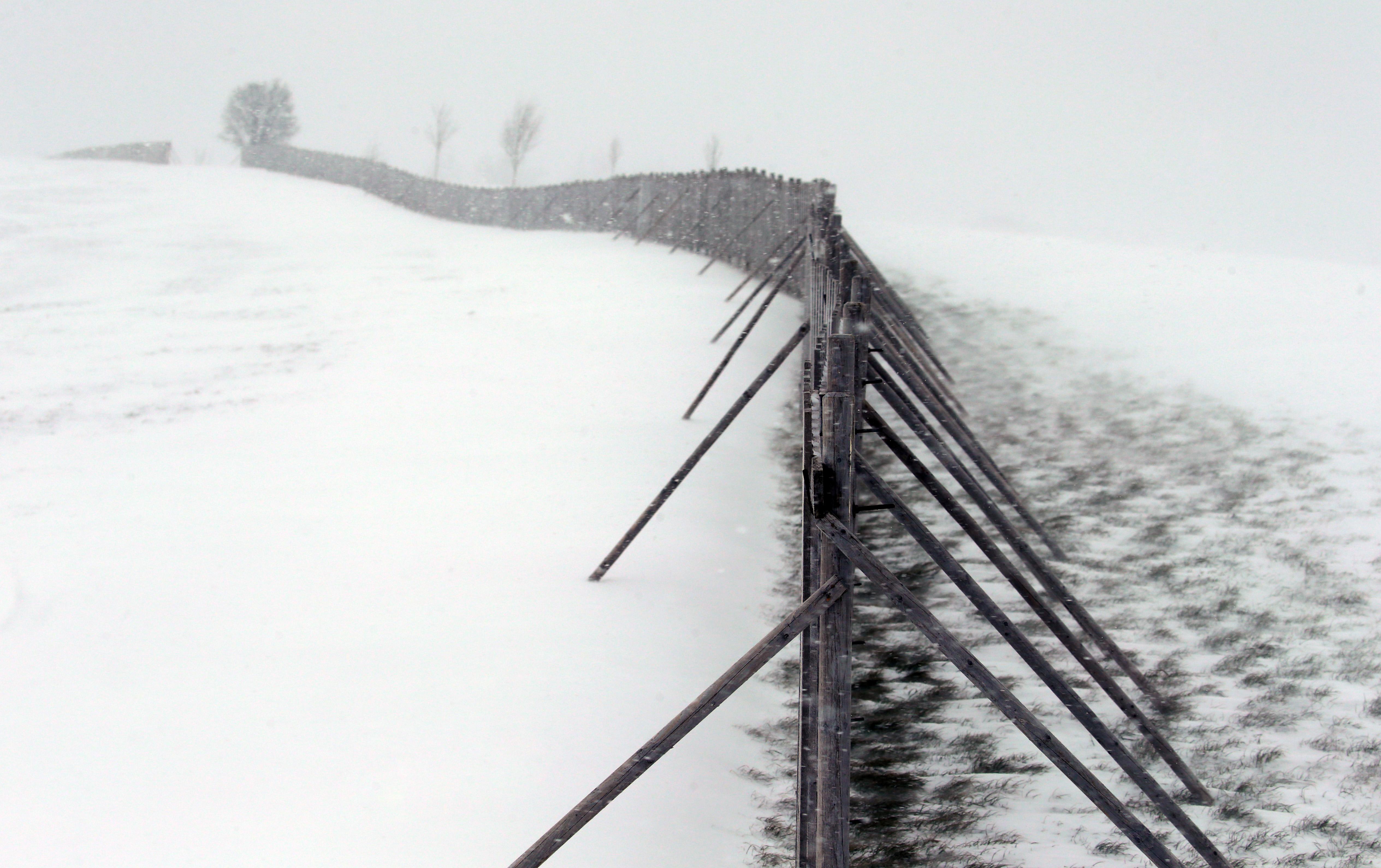 Heftiger Wind weht den Schnee in Lengenwang über einen Schneefangzaun. Dieser reduziert Schneeverwehungen und wird an diesem Wochenende besonders beansprucht.