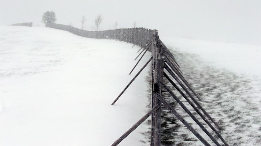 Heftiger Wind weht den Schnee in Lengenwang über einen Schneefangzaun. Dieser reduziert Schneeverwehungen und wird an diesem Wochenende besonders beansprucht.